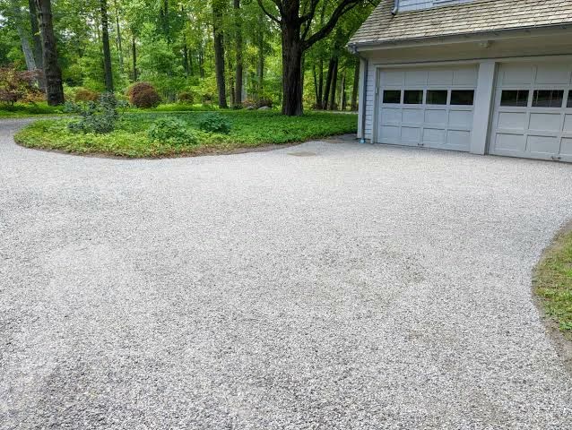 A freshly spread light gravel driveway in front of a two-door garage, a planted bed curving along one side.
